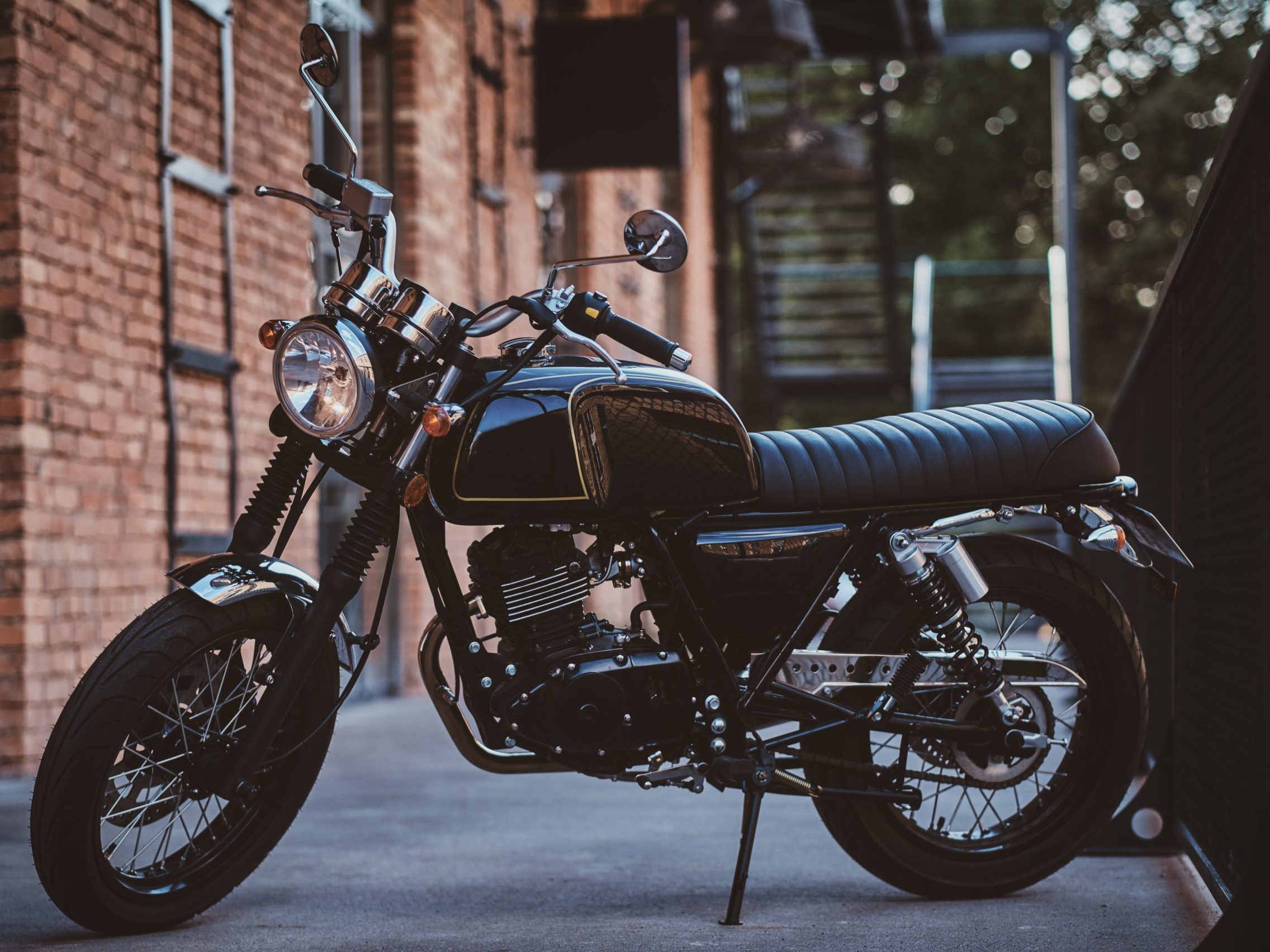 Brand new, shiny black retro chopper is parked next to brick building.